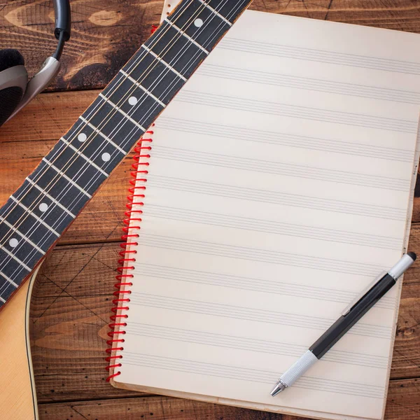 Buzuki, headphones and a clean musical note book on a wooden table, top view, musical concept, copy space