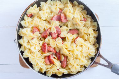 Adım adım pişirme makarna domates soslu peynirli, adım 4 - soslu makarna ve sosis, seçici odak, üstten görünüm karıştırma