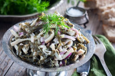 Deniz yosunu ve ahşap bir masa, seçici odak üzerinde metal bir tabak kalamar salatası
