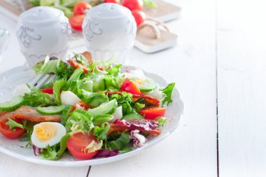 Salad of fresh herbs, fried bacon, cherry tomatoes, quail eggs on a white plate, horizontal, copy space clipart