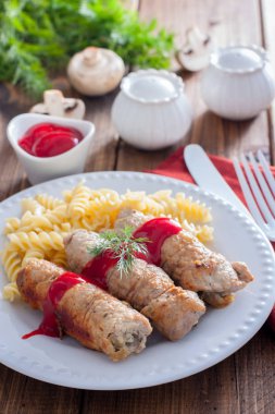 Küçük domuz makarna ve ketçap, seçici odak ile beyaz bir plaka üzerinde petrol ile rulo