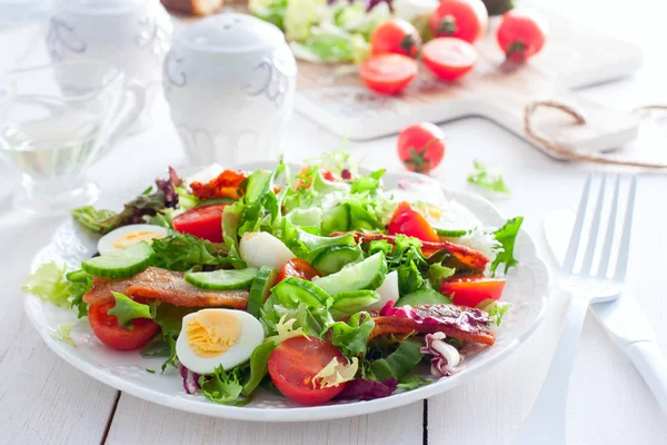 Salade fraîche de bacon rôti, tomates cerises, oeufs de caille sur une assiette blanche, horizontale — Photo