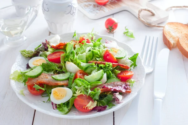 Salade fraîche de bacon rôti, tomates cerises, oeufs de caille sur une assiette blanche, horizontale — Photo