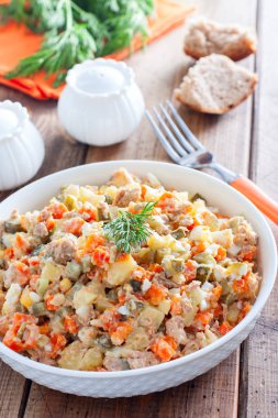 Ahşap bir masa, yatay üzerinde beyaz bir tabakta konserve ton balığı ile Rus salatası-İspanyolca