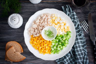 Mısır salatası, salatalık, yumurta, tavuk beyaz bir plaka üzerinde siyah bir masa, üst görünüm, yatay