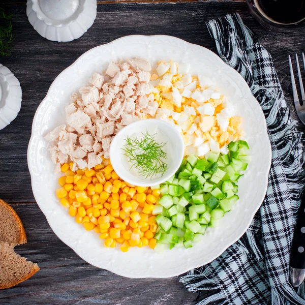 Кукурузный салат, огурец, яйцо, курица на белой тарелке на черном столе, вид сверху, квадрат — стоковое фото