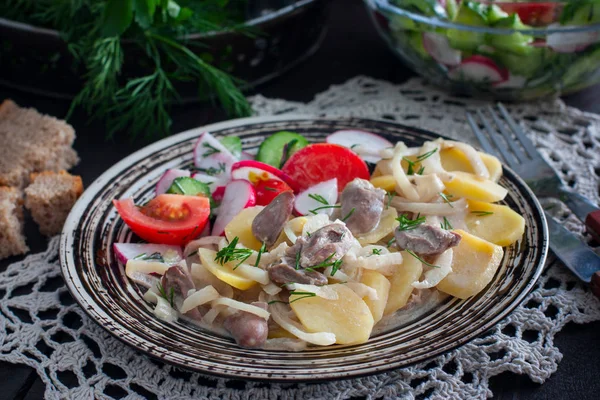 Cooked potatoes and chicken hearts on a plate with vegetable salad, horizontal