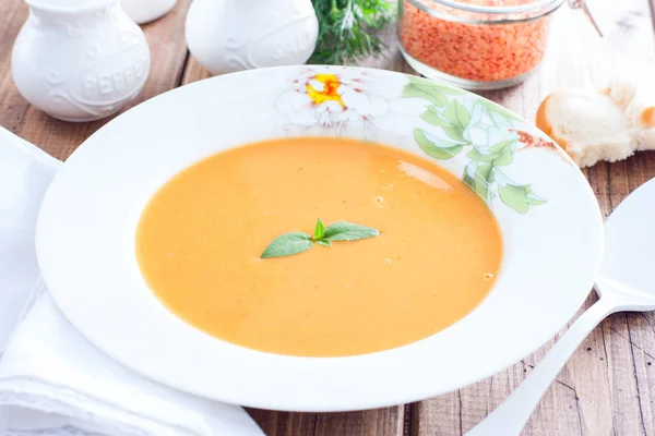 Red lentil cream soup in a white plate on a wooden table, horizontal — Stock Photo, Image