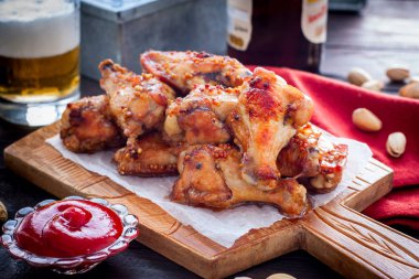 Domates sosu ve bir bardak bira ile ahşap bir tahta üzerinde pişmiş kanatlar, yatay
