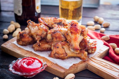 Domates sosu ve bir bardak bira ile ahşap bir tahta üzerinde pişmiş kanatlar, yatay