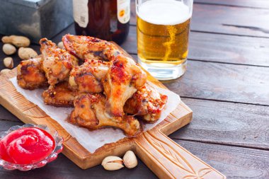 Domates sosu ve bir bardak bira ile ahşap bir tahta üzerinde pişmiş kanatlar, yatay, kopya alanı