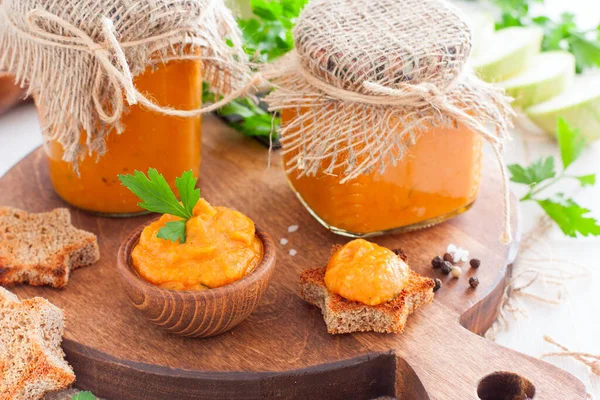 Homemade squash caviar in glass jars, gravy boat and on toast on wooden board, selective focus