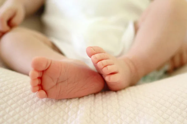 Tiny delicate feet of newborn baby on a bed.