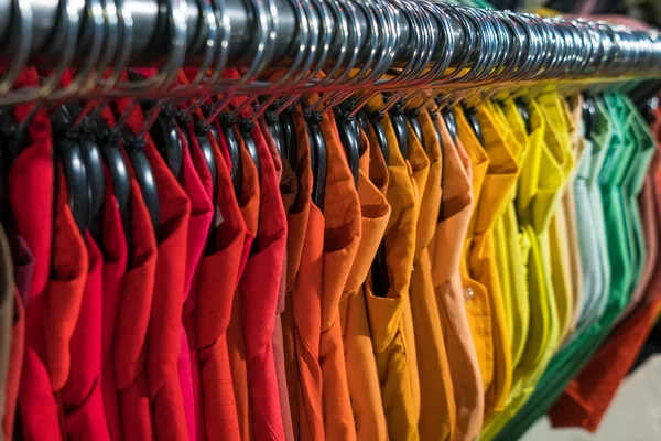 Male men shirts sorted in color order on hangers on a thrift shop or wardrobe closet rail