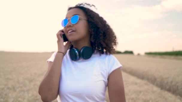 美しいスローモーション フォロー ショット ビデオ混合民族アフリカ系アメリカ人の女の子 シャツとブルーのサングラスを歩いて 彼女の携帯電話で話している若い女性 — ストック動画