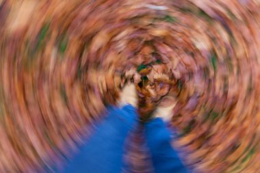 Motion blurred photograph of man or womans feet walking through golden Fall or Autumn leaves clipart