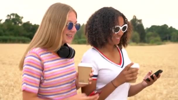 慢动作跟踪视频剪辑漂亮的金发女孩和混合种族十几岁的年轻妇女戴墨镜喝咖啡和使用手机手机 — 图库视频影像