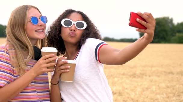 かなりブロンドの女の子と飲むコーヒーと撮影 Selfies 彼らのスマート フォンでサングラスをかけて混血ティーンエイ ジャー若い女性のスロー モーション ビデオ クリップ — ストック動画