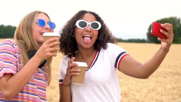 慢动作视频剪辑漂亮的金发女孩和混合种族青少年年轻妇女戴墨镜喝咖啡 并采取自拍在他们的智能手机 — 图库视频影像