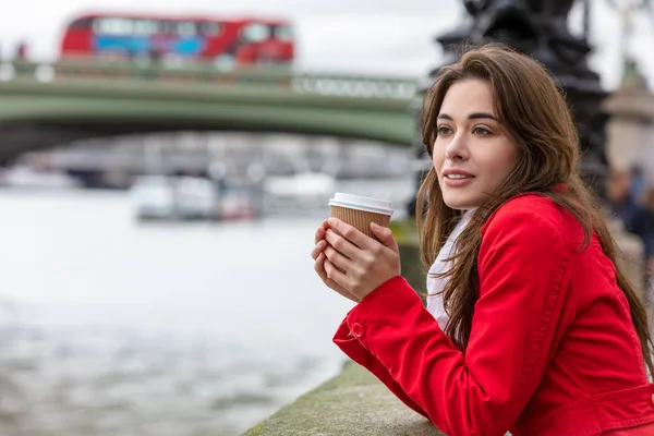 ロンドン イングランド イギリスの赤い 階建てバスでウェストミン スター橋の横にある使い捨てカップでコーヒーを飲む赤いコートの少女や若い女性 — ストック写真