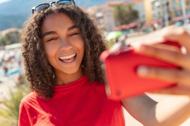 Beautiful happy mixed race African American young woman girl teenager female child smiling with perfect teeth taking selfie photograph with red cell phone clipart