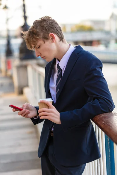 身に着けているスーツとネクタイ ソーシャル メディアのスマート携帯電話を使用して テイクアウトのコーヒーを飲みながら男性の若い大人のティーンエイ ジャー — ストック写真