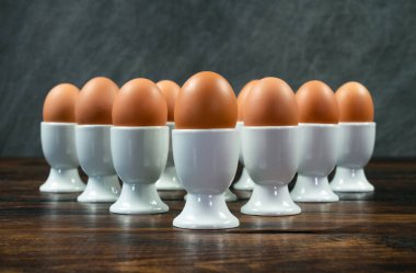 Ten boiled eggs in white egg cups on a wooden table in a triangle arrangement clipart