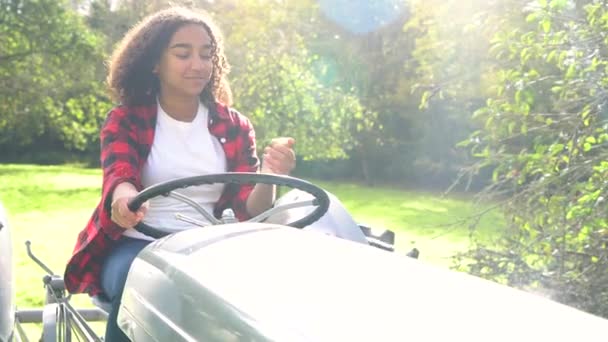 美丽的非裔美国人混合种族少女少女驾驶一辆灰色拖拉机通过一个阳光明媚的苹果园吃一个苹果 — 图库视频影像