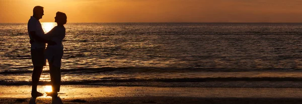 愉快的资深男人和女人夫妇一起拥抱拥抱在日落在一个废弃的热带海滩全景网络横幅 — 图库照片