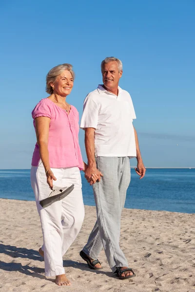 幸せなシニア男性と女性のカップルを笑みを浮かべて歩いて手を繋いでいる明るいと捨てられた熱帯ビーチでバカンス澄んだ青い空と海を静める — ストック写真