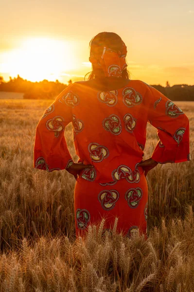 Mujer africana con ropa tradicional de pie en un campo de cultivos al atardecer o al amanecer —  Fotos de Stock