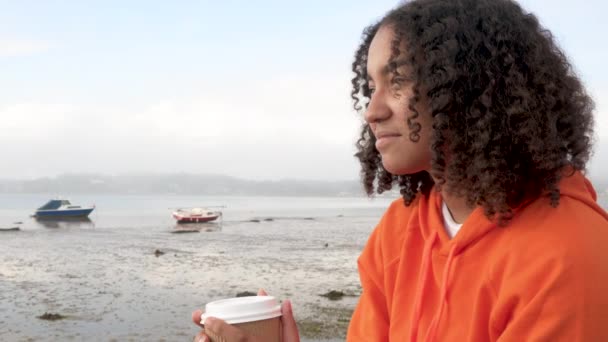 漂亮的混血非洲裔美国少女 身穿橙色帽衫 在港口边喝着外卖咖啡 面带微笑 笑逐颜开 — 图库视频影像