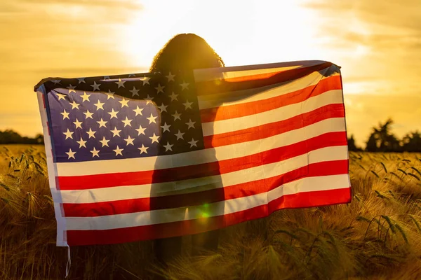 Meisje tiener verpakt in Usa vlag in veld bij zonsondergang — Stockfoto