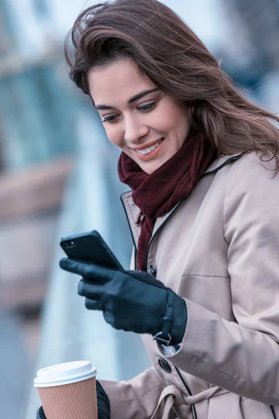 Frau trinkt Kaffee und sucht Handy an einem kalten Tag in einer Stadt — Stockfoto