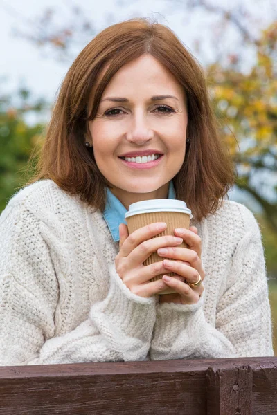 Atrakcyjna szczęśliwa Kobieta w średnim wieku spoczywającej na ogrodzeniu z kawą — Zdjęcie stockowe