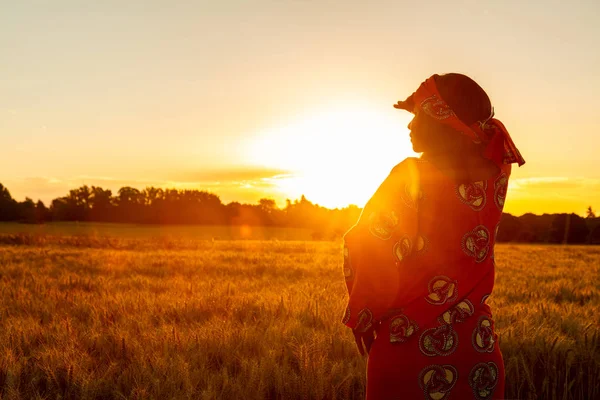 Africká žena v tradičním oblečení stojící v oblasti plodin při západu slunce nebo sunrise — Stock fotografie