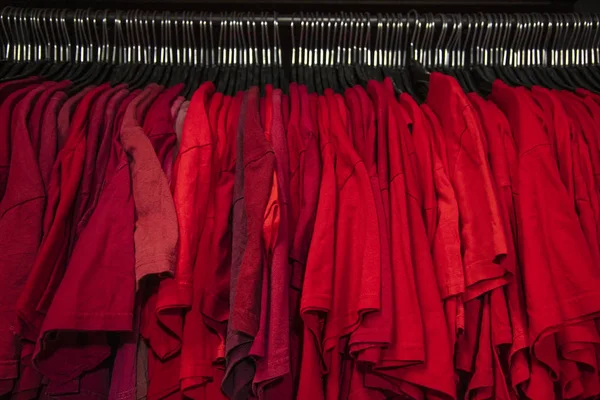 Czerwone T-shirty na wieszakach na szafie sklepu szafy szyna — Zdjęcie stockowe
