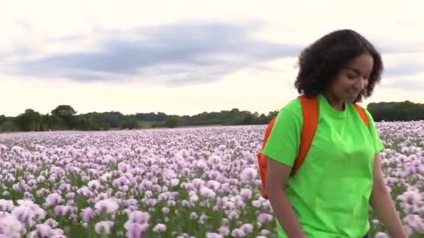 美丽的快乐混合种族非洲裔美国少女少女女青年徒步旅行与橙色背包通过粉红色罂粟花领域路径 — 图库视频影像