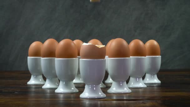 在木制桌子上的一群戴着白色蛋杯的鸡蛋前面 一个人把一个吐司士兵泡在一个煮熟的鸡蛋里 — 图库视频影像