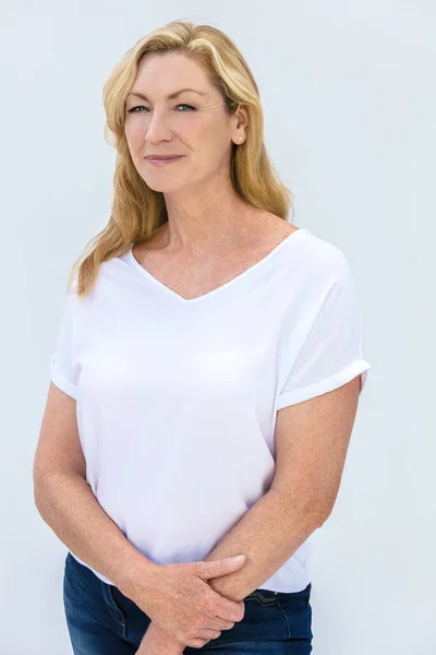 一个漂亮的中年金发女人穿着白色T恤和蓝色牛仔裤在白色背景上微笑的工作室肖像 — 图库照片
