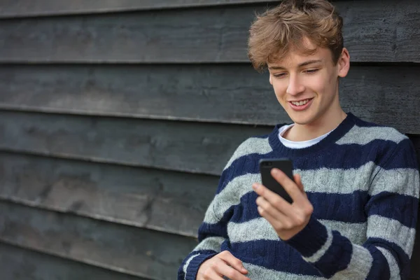 笑顔幸せな男の子ティーン外の傾き壁使用して彼の携帯電話のための彼の携帯電話のソーシャルメディアやビデオ通話 — ストック写真