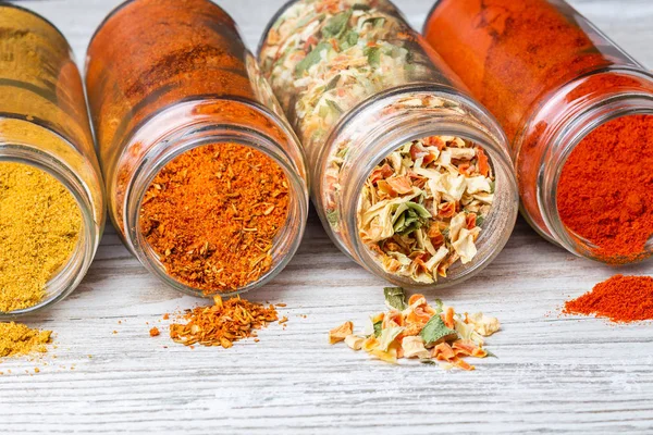 Ahşap bir tezgahın üzerinde duran kavanozlardan dökülen baharatlar. dondurulmuş kurutulmuş sebze, zemin kırmızı biber, köri ve baharat karışımları.