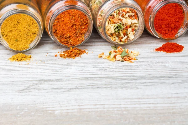 Yalan söyleyen kavanozlardan dökülen renkli baharatlar. Ahşap bir tezgah üzerinde baharatlar ve boş alan. Lyophilized sebze, zemin kırmızı biber, köri ve baharat karışımı.