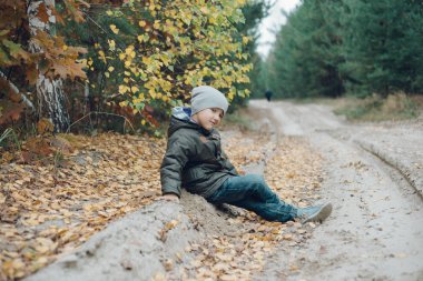 Çocuk sonbahar ormanında yerde oynuyor. 