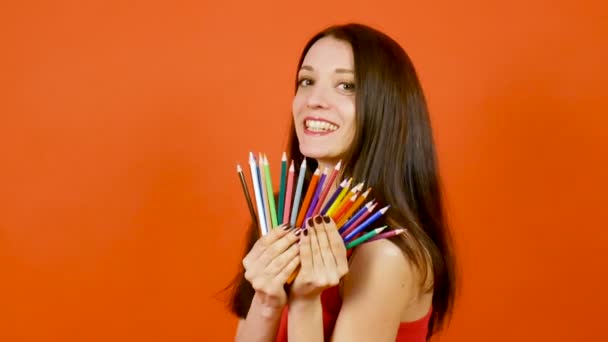 Junge brünette Frau mit bunten Bleistiften, die auf orangefarbenem Hintergrund posiert. Art Design Konzept — Stockvideo