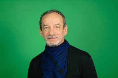 Yakışıklı üst düzey gri saçlı adam siyah kazak ve mavi etmek eşarp çevresinde Well-trimmed sakallı onun boyun seyir Studio yeşil arka plan üzerinde kamera