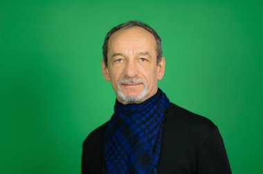 Stüdyo portre bir üst düzey gri saçlı adam siyah kazak ve mavi etmek eşarp çevresinde Well-trimmed sakallı onun boyun arıyorum yeşil arka plan üzerinde kamera