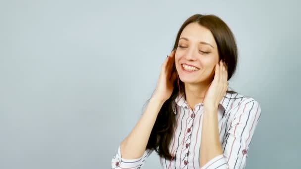 Hermosa morena sonriente escucha música usando auriculares en el estudio sobre fondo gris . — Vídeo de stock