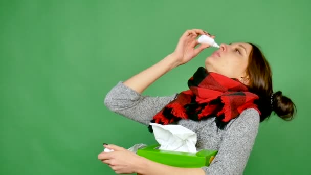 Porträt einer attraktiven Brünetten mit Grippe. das Mädchen hat eine Erkältung, Fieber, der Hals ist in einen Schal gewickelt. sie gräbt Nase mit Tropfen für die Nase — Stockvideo