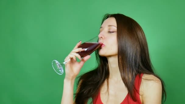 Schöne Mädchen lächelt und hebt ein Glas Wein in Toast. Sie trägt ein rotes Trikot. grüner Hintergrund — Stockvideo